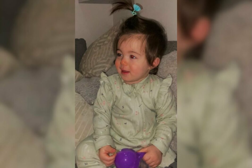 Imagem colorida de bebê sentado com brinquedo roxo olhando para o lado com reflexo nos olhos - Metrópoles